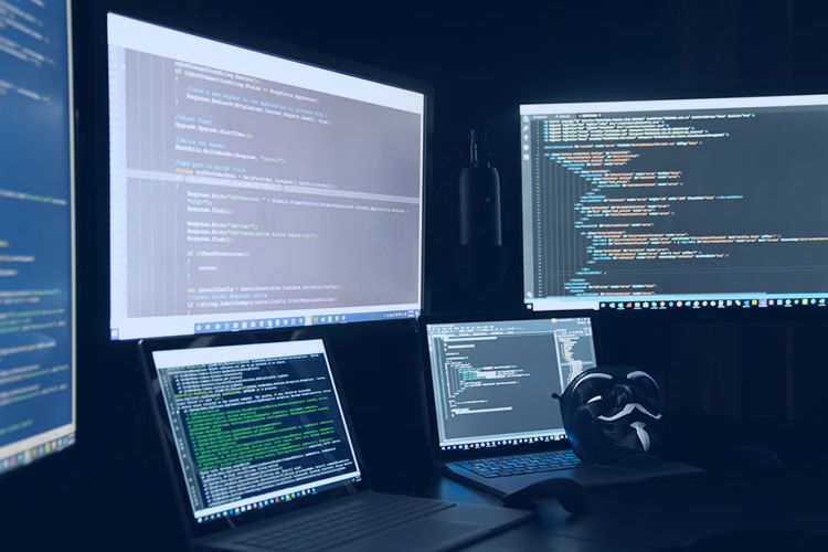 Estação de trabalho com múltiplos monitores exibindo códigos de programação em uma sala escura, destacando um ambiente típico de desenvolvimento de software.