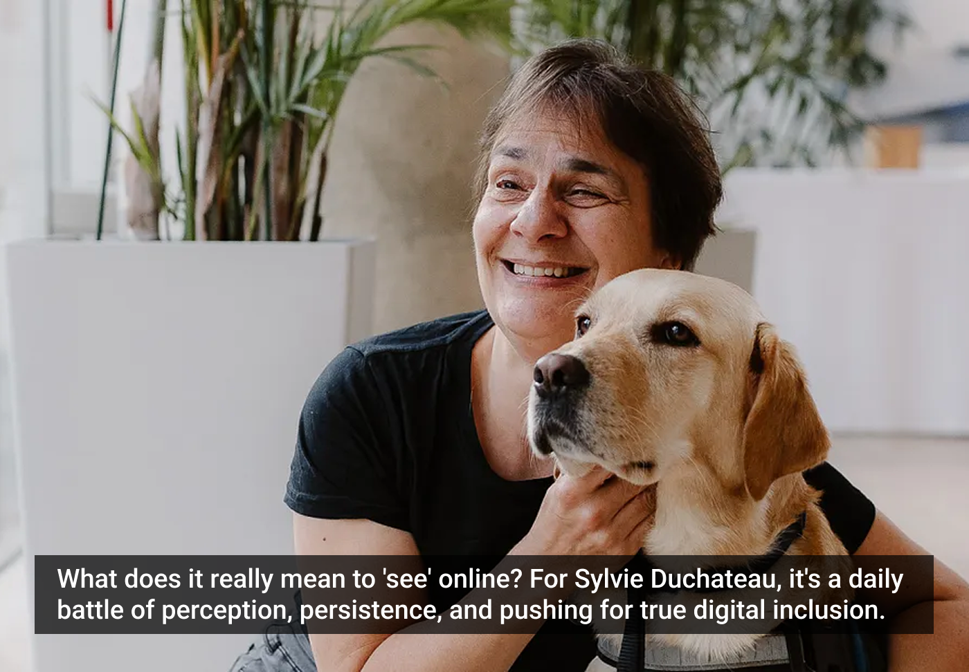 Mulher sorridente abraça labrador bege em ambiente interno com plantas ao fundo.