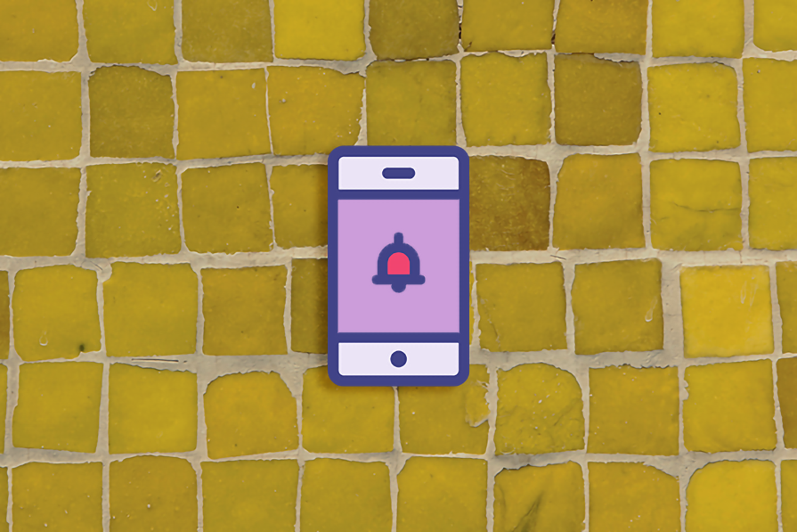 Smartphone com ícone de notificação sobre uma superfície de ladrilhos amarelos desgastados.