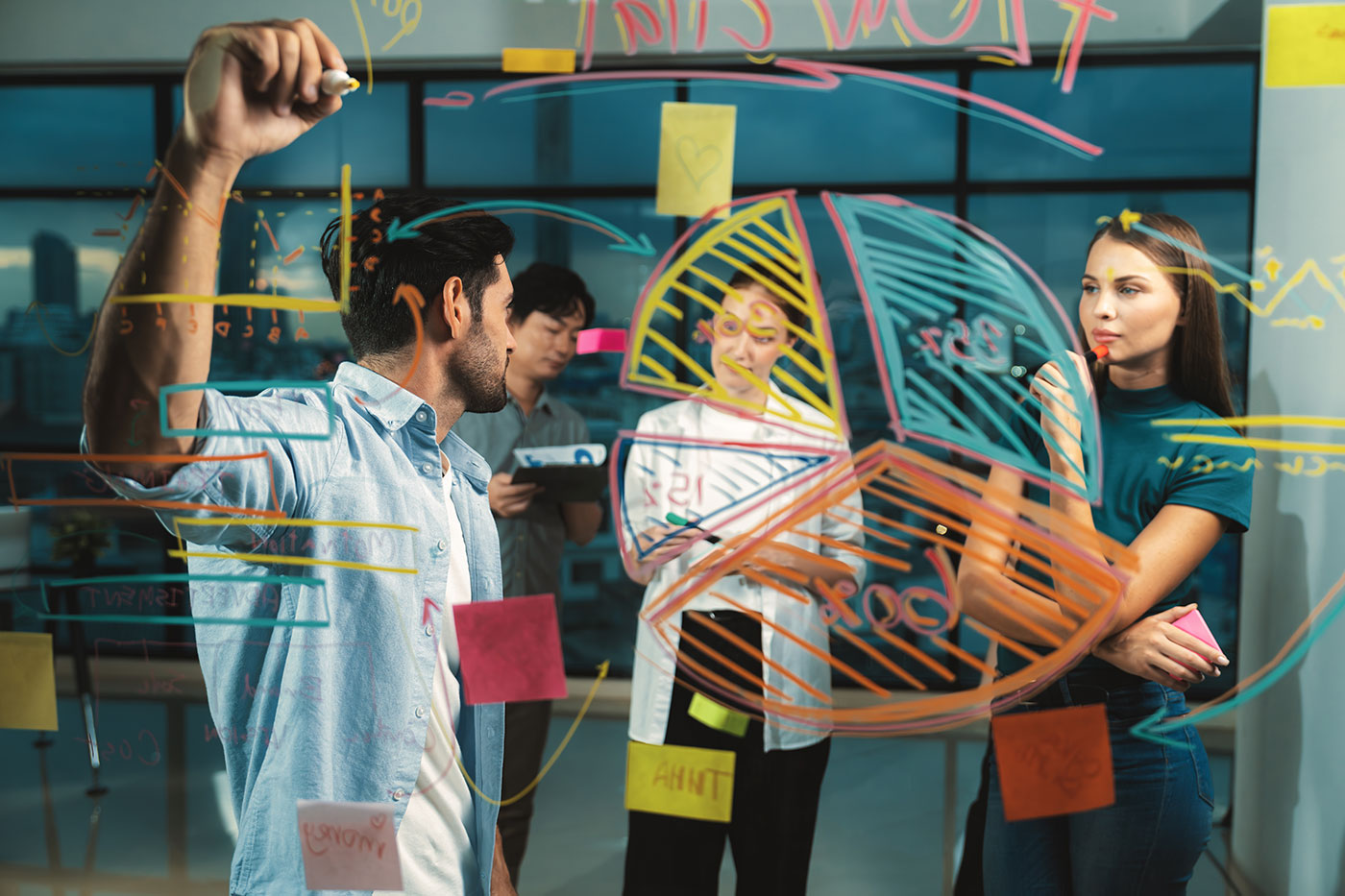 Quatro colegas trabalhando juntos em um painel de vidro coberto de gráficos coloridos e notas adesivas. Eles discutem e anotam ideias ativamente.